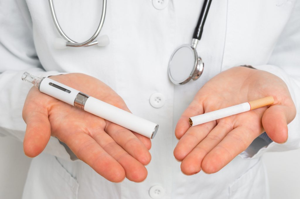 Un médecin tient une cigarette de tabac dans sa main, et une cigarette électronique dans l'autre