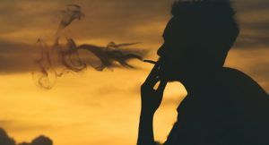Homme fumant une cigarette sur un coucher de soleil
