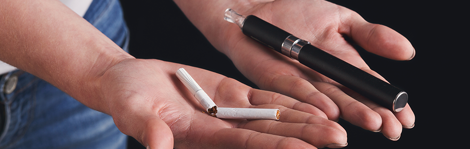 Une femme tient une cigarette électronique dans une main et des cigarettes de tabac dans l'autre
